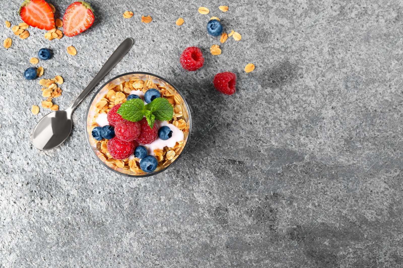 Photo of Glass of healthy homemade granola dessert on grey table, flat lay. Space for text