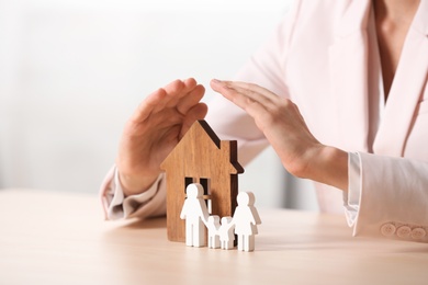 Female agent covering wooden house and family at table, closeup. Home insurance