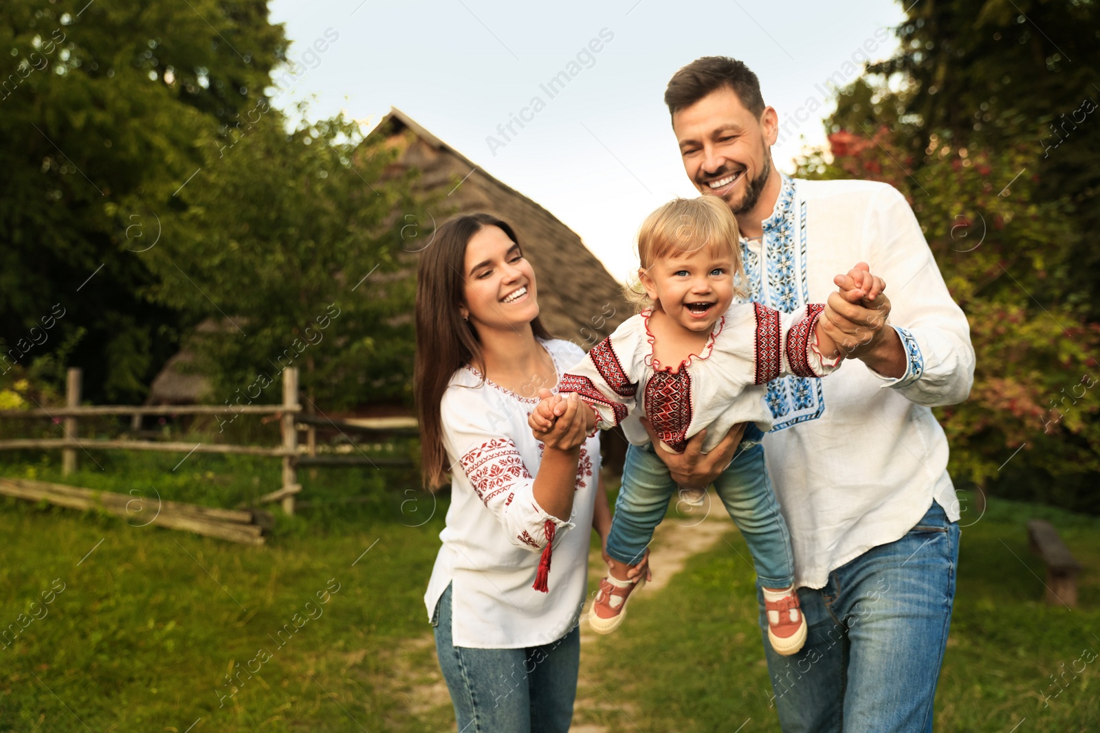 Photo of Happy cute family playing in embroidered Ukrainian shirts near house on sunny day. Space for text