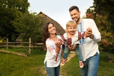 Photo of Happy cute family playing in embroidered Ukrainian shirts near house on sunny day. Space for text