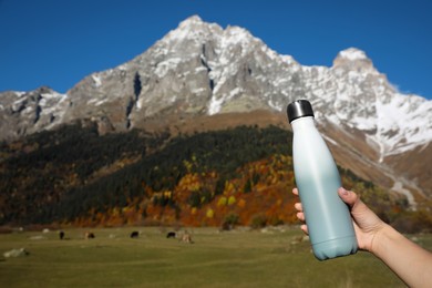 Woman holding thermo bottle with drink in mountains on sunny day. Space for text