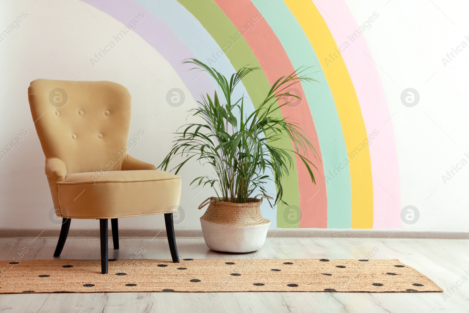 Photo of Comfortable chair, runner rug and houseplant near white wall with rainbow art indoors