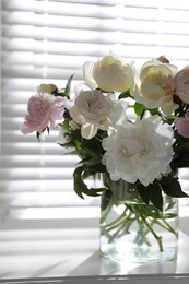 Beautiful peonies in vase on table near window indoors