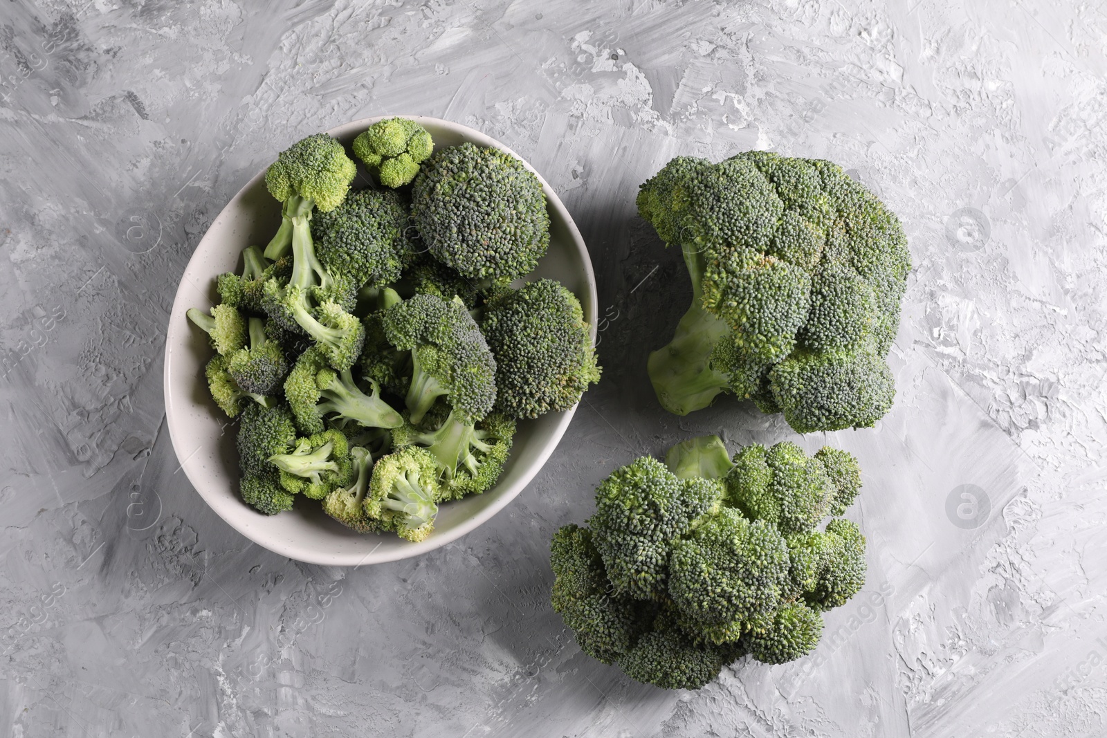 Photo of Bowl of fresh raw broccoli on grey textured table, flat lay