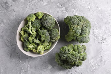 Bowl of fresh raw broccoli on grey textured table, flat lay