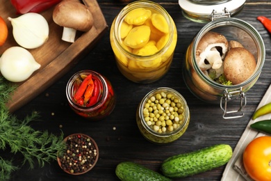 Photo of Jars with pickled vegetables on black wooden table, flat lay