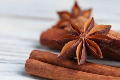 Photo of Aromatic anise stars and cinnamon sticks on white wooden table, closeup