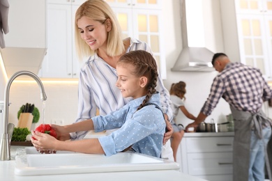 Little girl with her mother washing vegetables together in modern kitchen