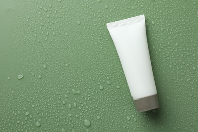 Moisturizing cream in tube on green background with water drops, top view. Space for text