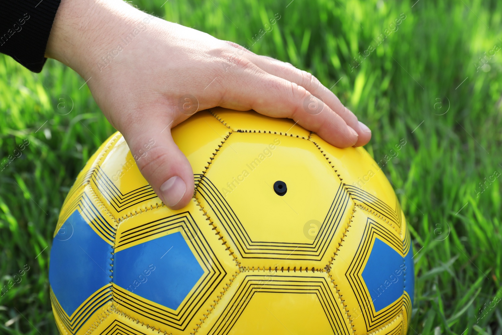 Photo of Man holding yellow soccer ball on green grass, closeup