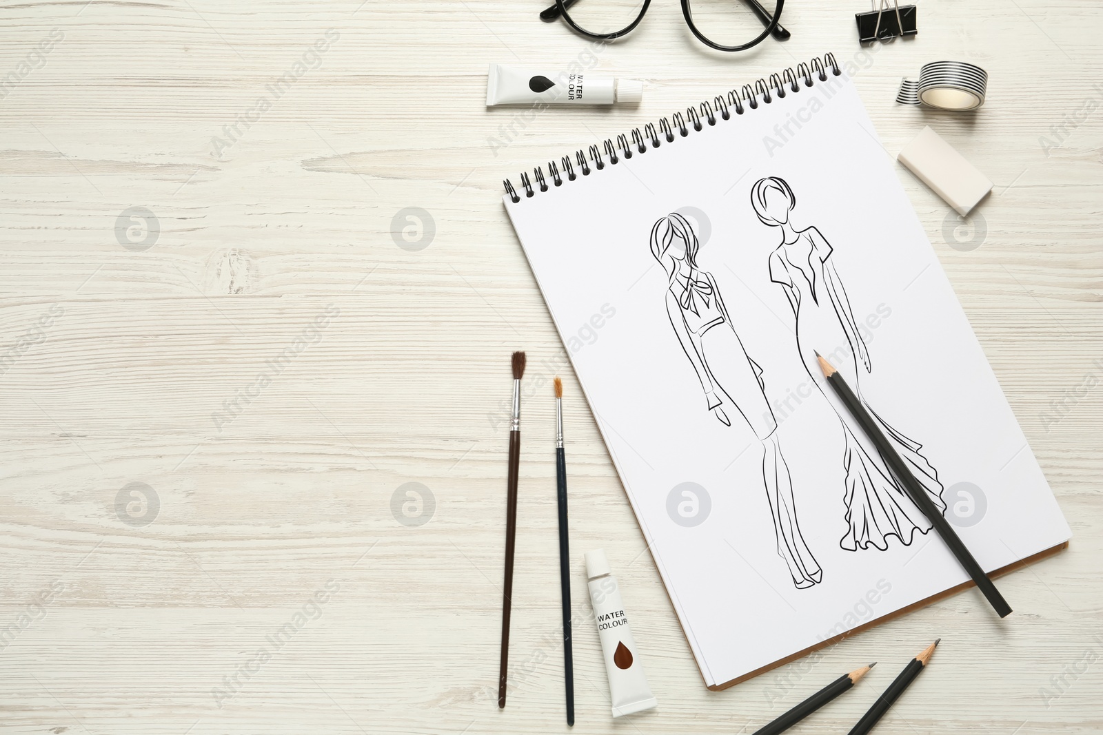 Image of Sketches of different clothes in pad on white wooden table, space for text. Fashion designer's desk with stationery, flat lay