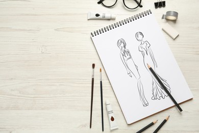 Image of Sketches of different clothes in pad on white wooden table, space for text. Fashion designer's desk with stationery, flat lay