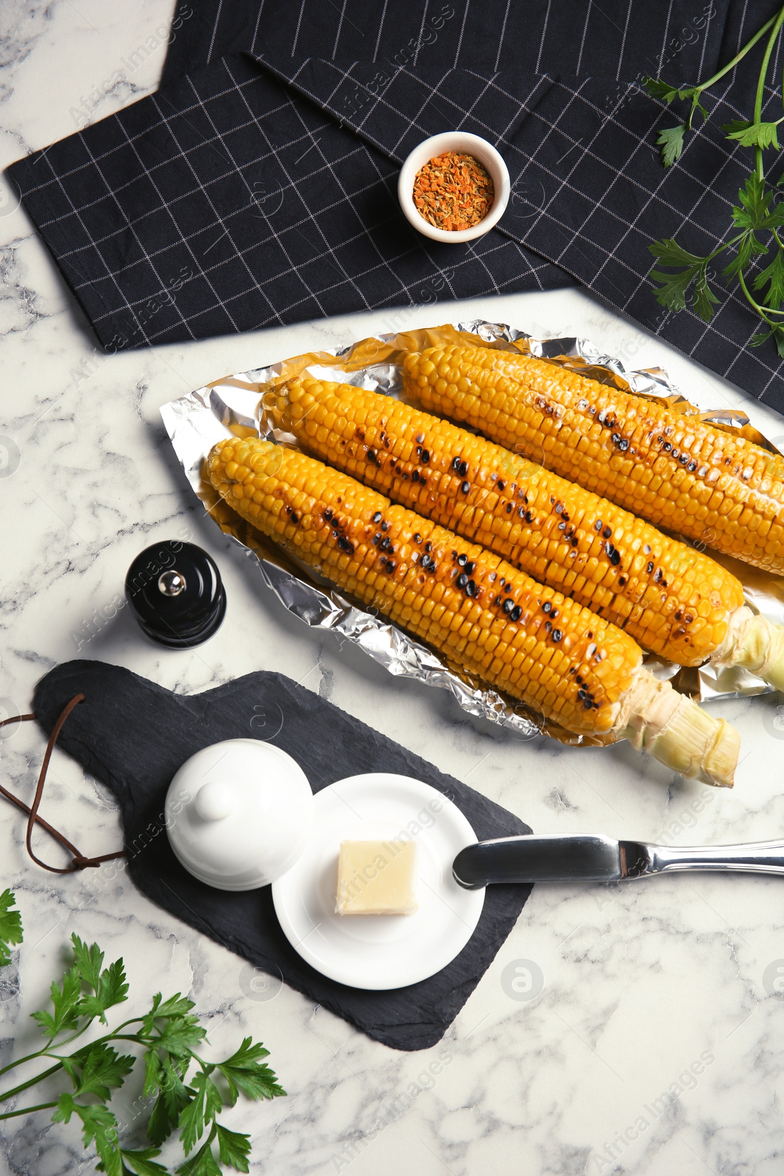 Photo of Fresh grilled tasty corn cobs served with butter on marble table, top view