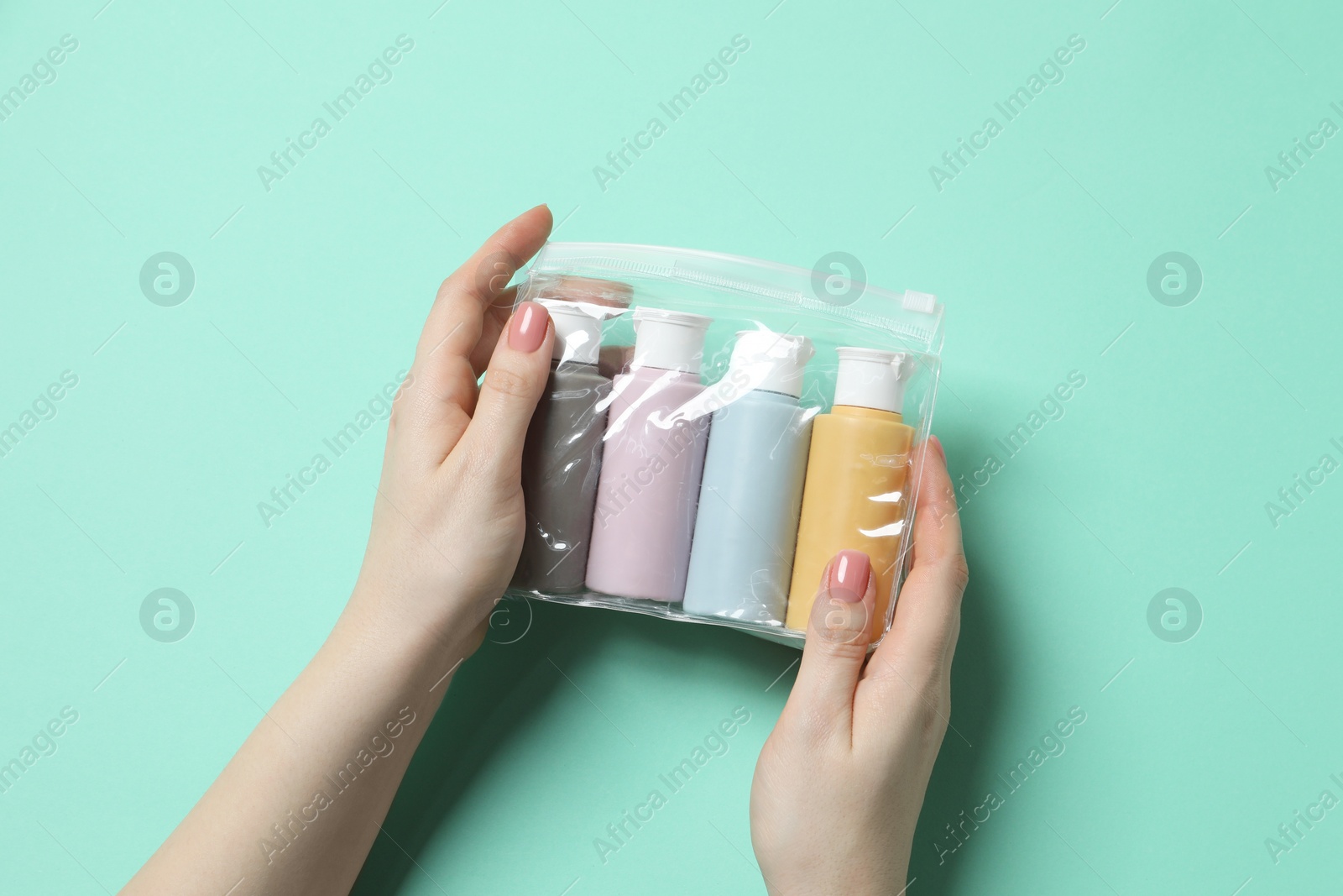 Photo of Cosmetic travel kit. Woman holding plastic bag with small bottles of personal care products against turquoise background, top view