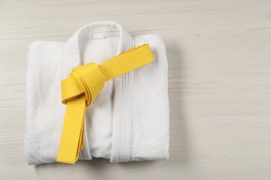 Photo of Yellow karate belt and white kimono on wooden background, top view. Space for text