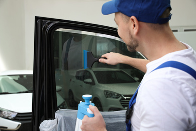 Worker washing tinted car window in workshop