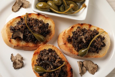 Photo of Delicious bruschettas with truffle sauce and caperberries on white plate, flat lay