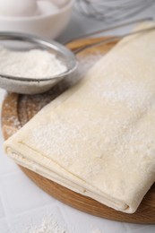 Photo of Raw puff pastry dough on white tiled table, closeup