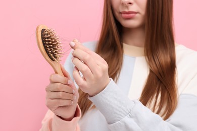 Photo of Woman untangling her lost hair from brush on pink background, closeup. Alopecia problem