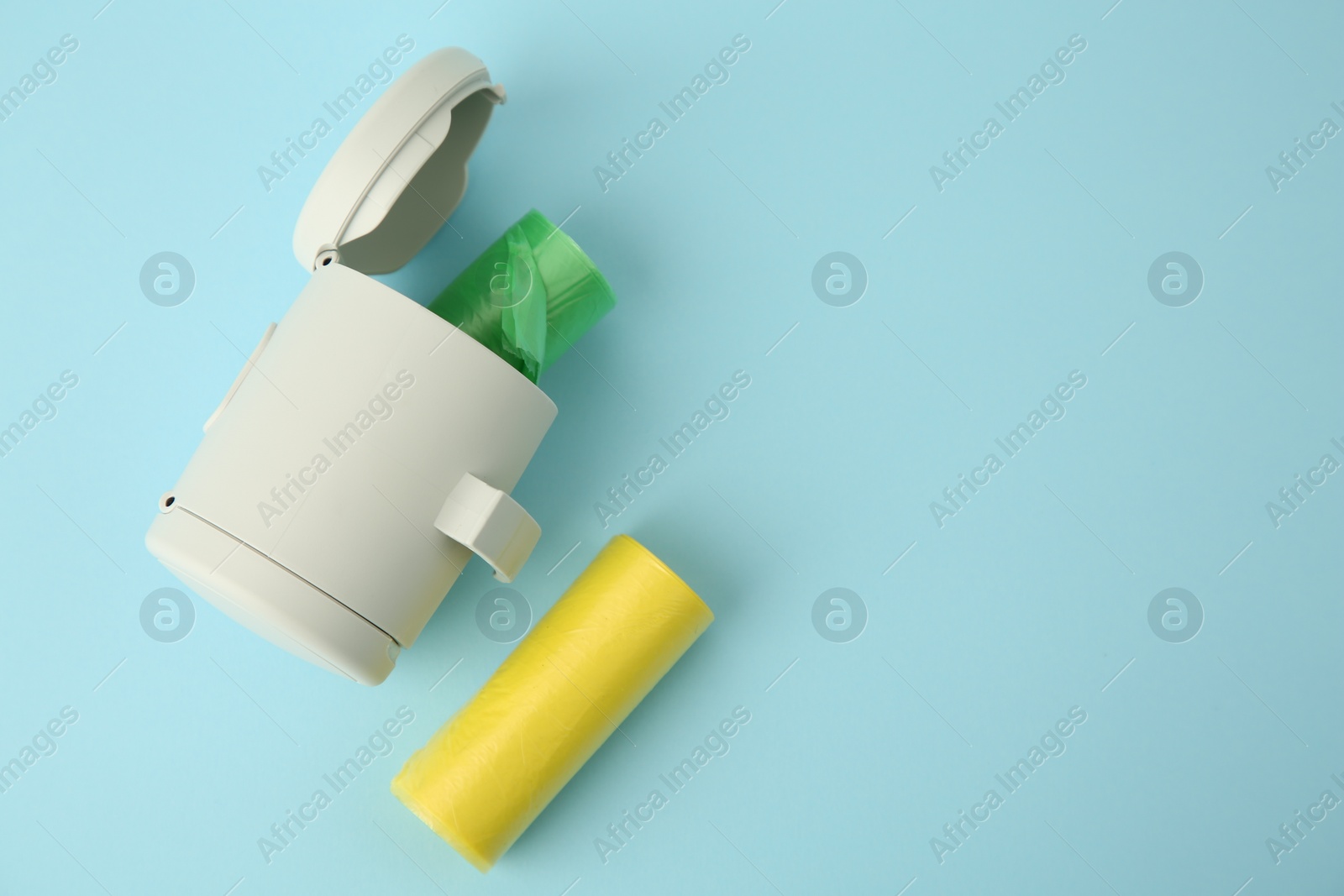 Photo of Dog waste bags and dispenser on light blue background, flat lay. Space for text