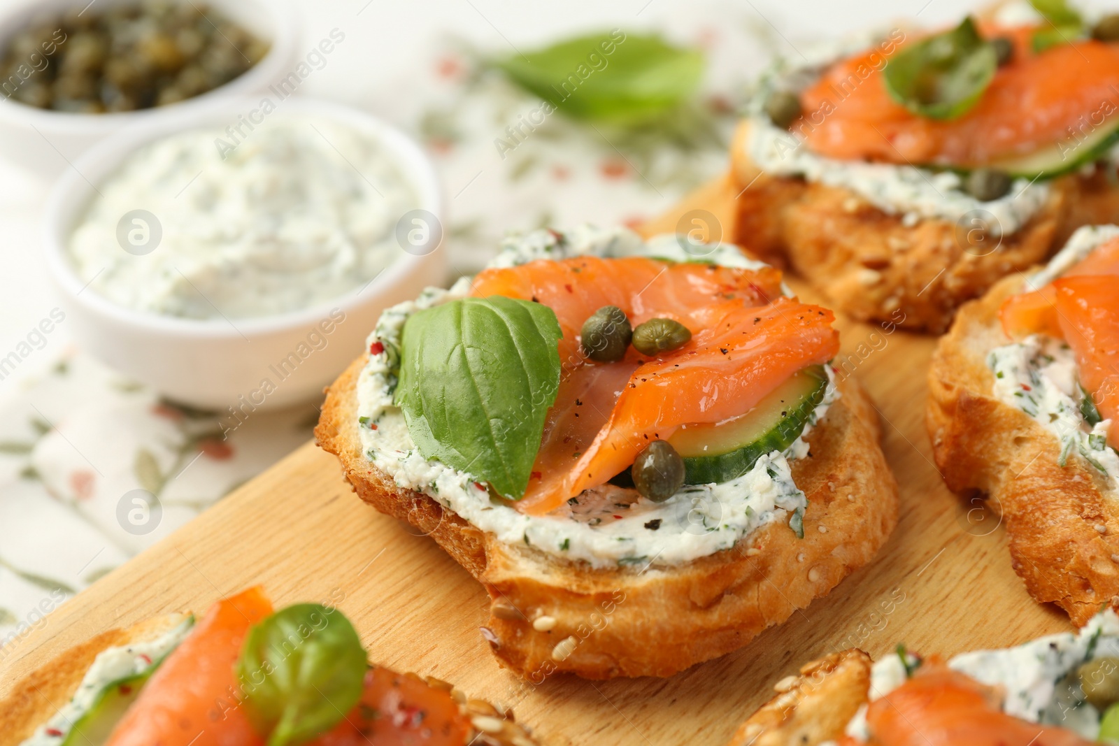 Photo of Tasty canapes with salmon, capers, cucumber and sauce on table, closeup