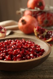 Ripe juicy pomegranate grains in bowl on wooden table, closeup