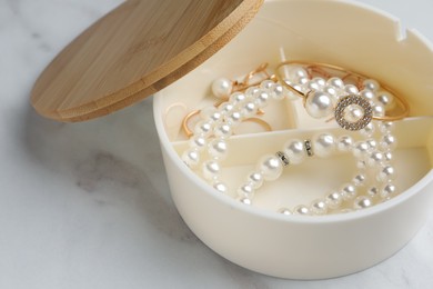 Stylish jewelry with pearls in box on white marble table, closeup view