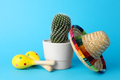 Photo of Mexican sombrero hat, cactus and maracas on light blue background