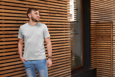 Photo of Young man wearing gray t-shirt near wooden wall on street. Urban style