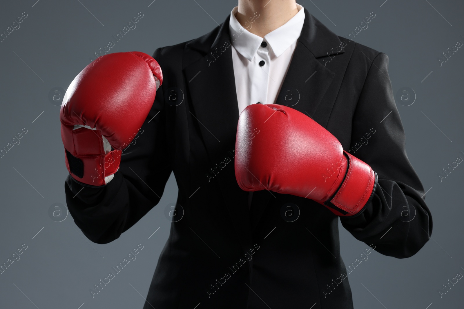 Photo of Businesswoman in suit wearing boxing gloves on grey background, closeup