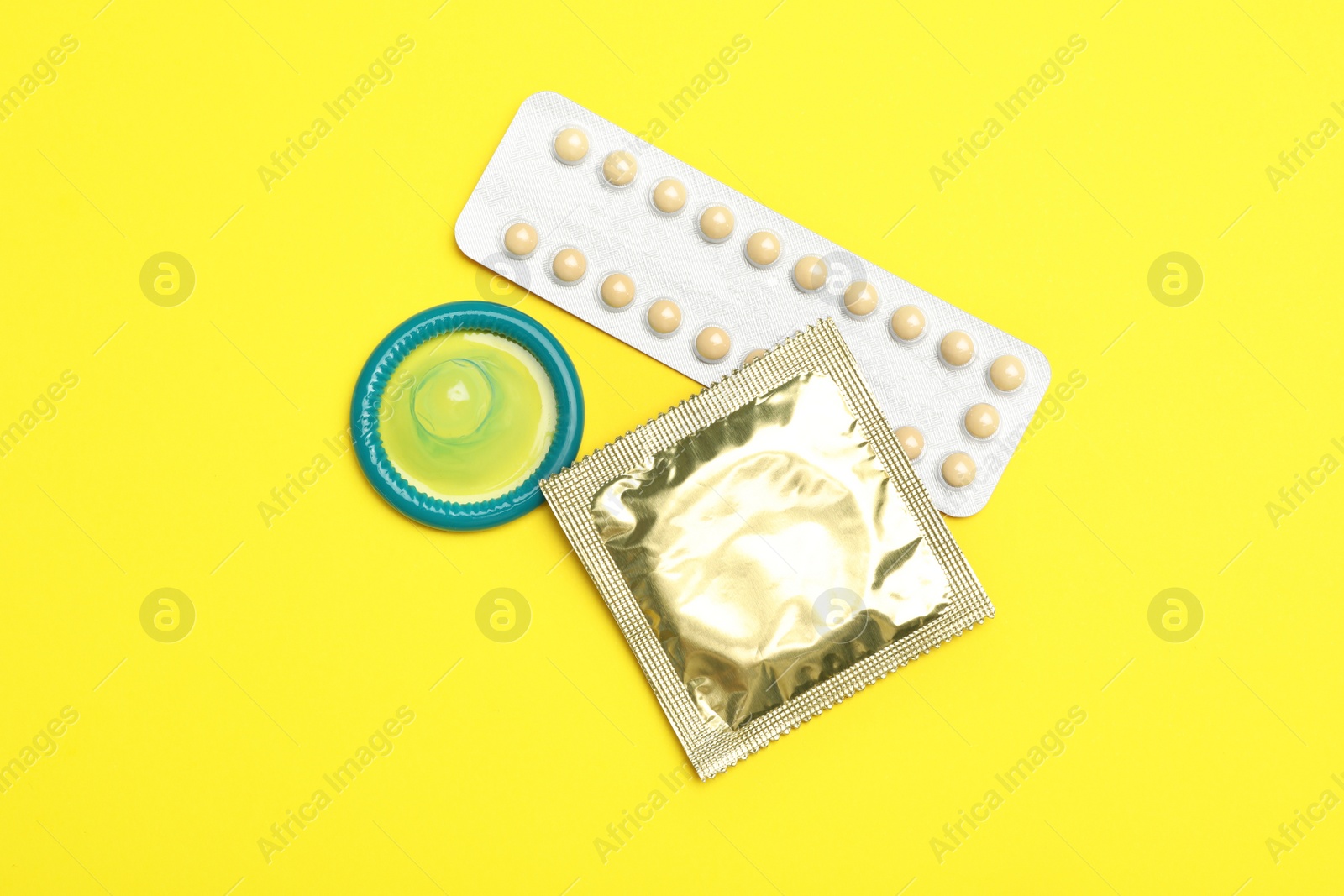 Photo of Condoms and birth control pills on yellow background, flat lay. Safe sex concept