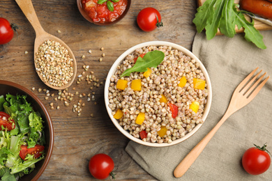 Photo of Tasty buckwheat porridge with vegetables on wooden table, flat lay