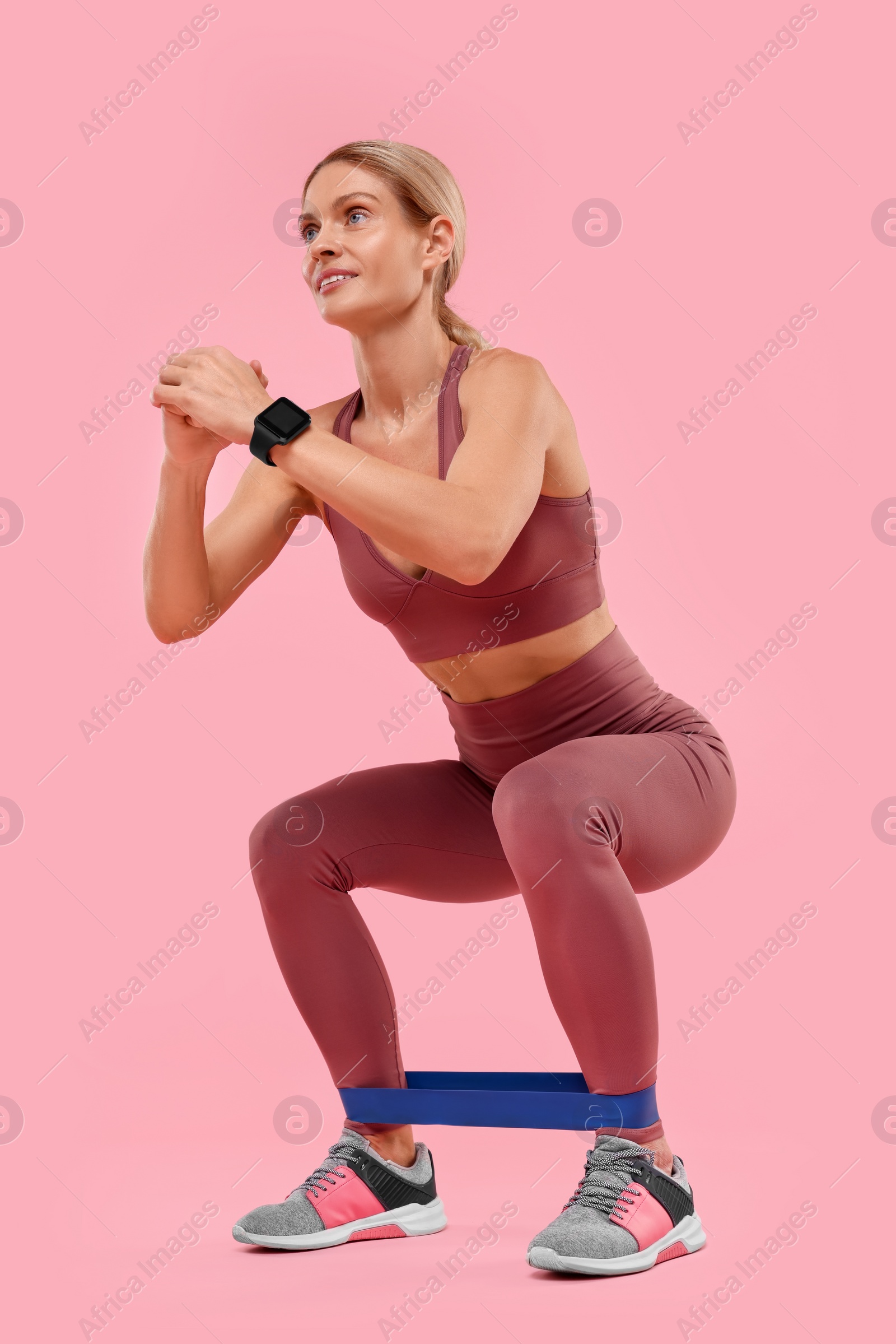 Photo of Woman exercising with elastic resistance band on pink background, low angle view