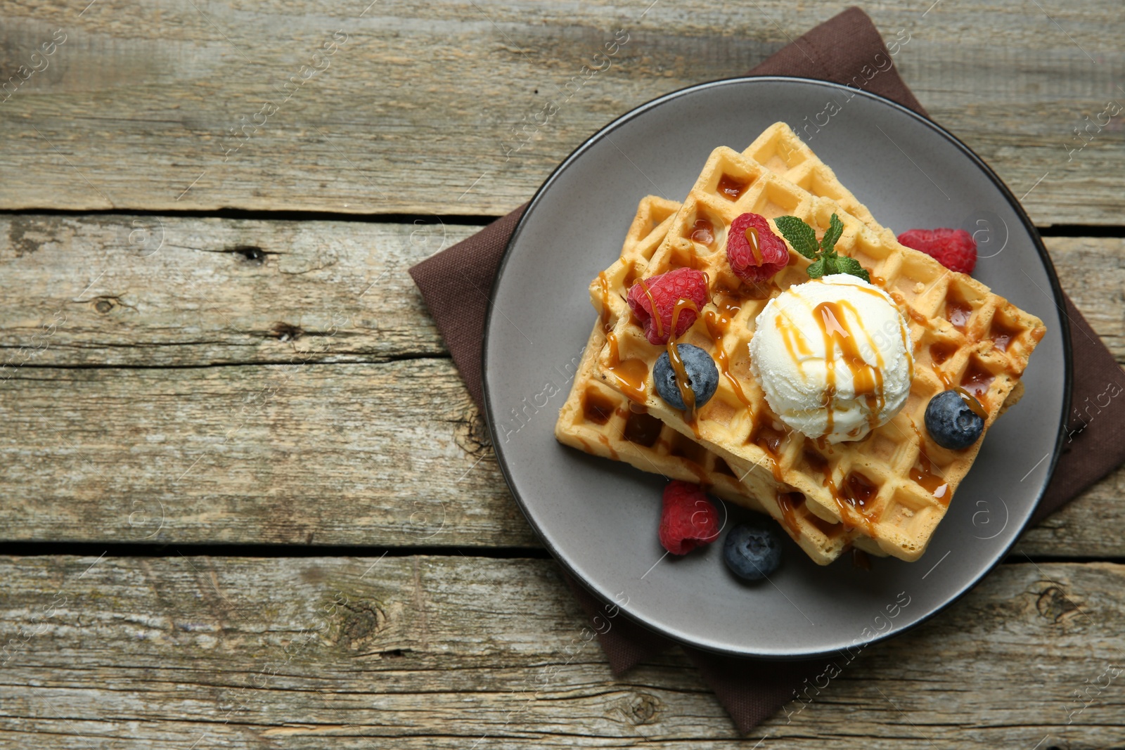 Photo of Delicious Belgian waffles with ice cream, berries and caramel sauce on wooden table, top view. Space for text