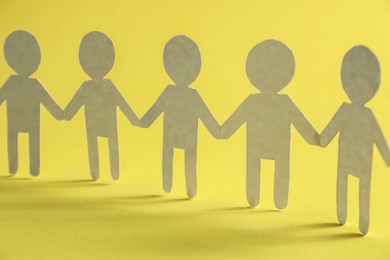 Photo of Teamwork concept. Paper figures of people holding hands on yellow background, closeup