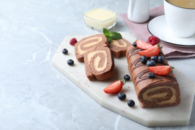 Tasty chocolate cake roll with cream and berries on light grey marble table. Space for text