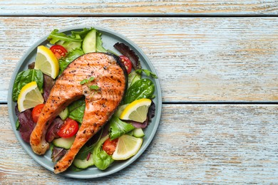 Photo of Tasty salmon steak with lemon and vegetables on white wooden table, top view. Space for text