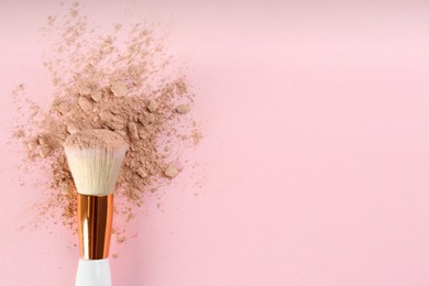 Makeup brush and scattered face powder on pink background, top view. Space for text