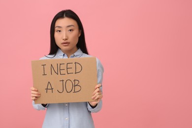 Unemployed Asian woman holding sign with phrase I Need A Job on pink background. Space for text