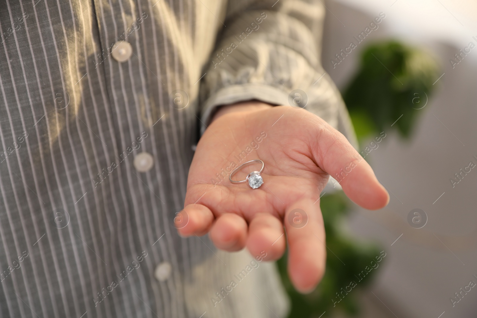 Photo of Woman holding wedding ring indoors, closeup. Divorce concept