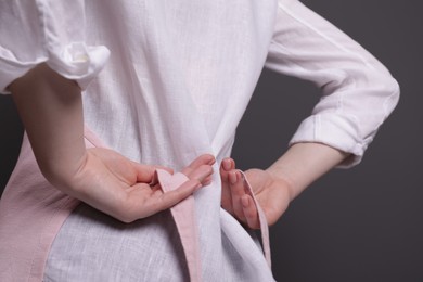 Photo of Woman putting on pink apron against grey background, closeup