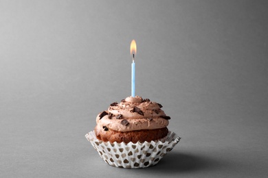 Chocolate cupcake with burning candle on grey background