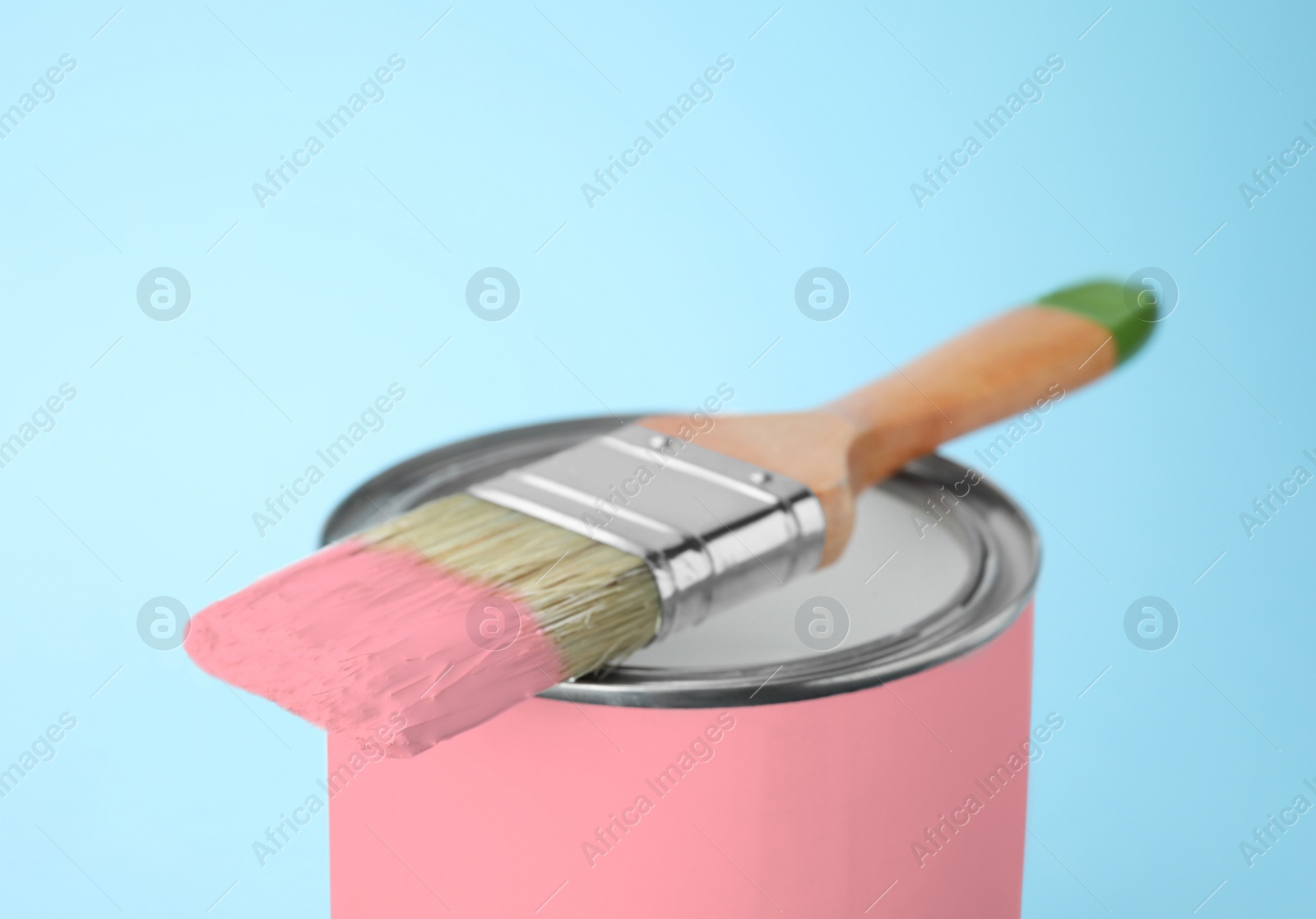 Photo of Can of pink paint with brush on blue background