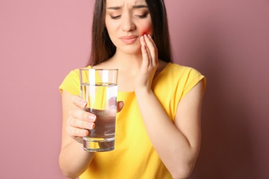 Woman with sensitive teeth holding glass of water on color background