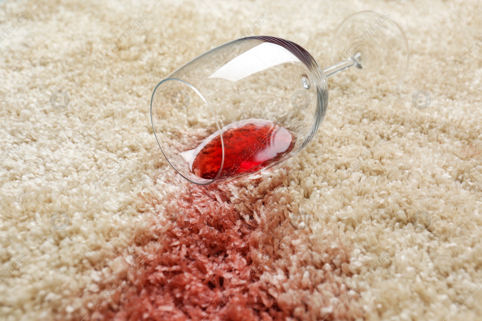 Photo of Overturned glass and spilled red wine on soft carpet, closeup