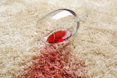 Photo of Overturned glass and spilled red wine on soft carpet, closeup