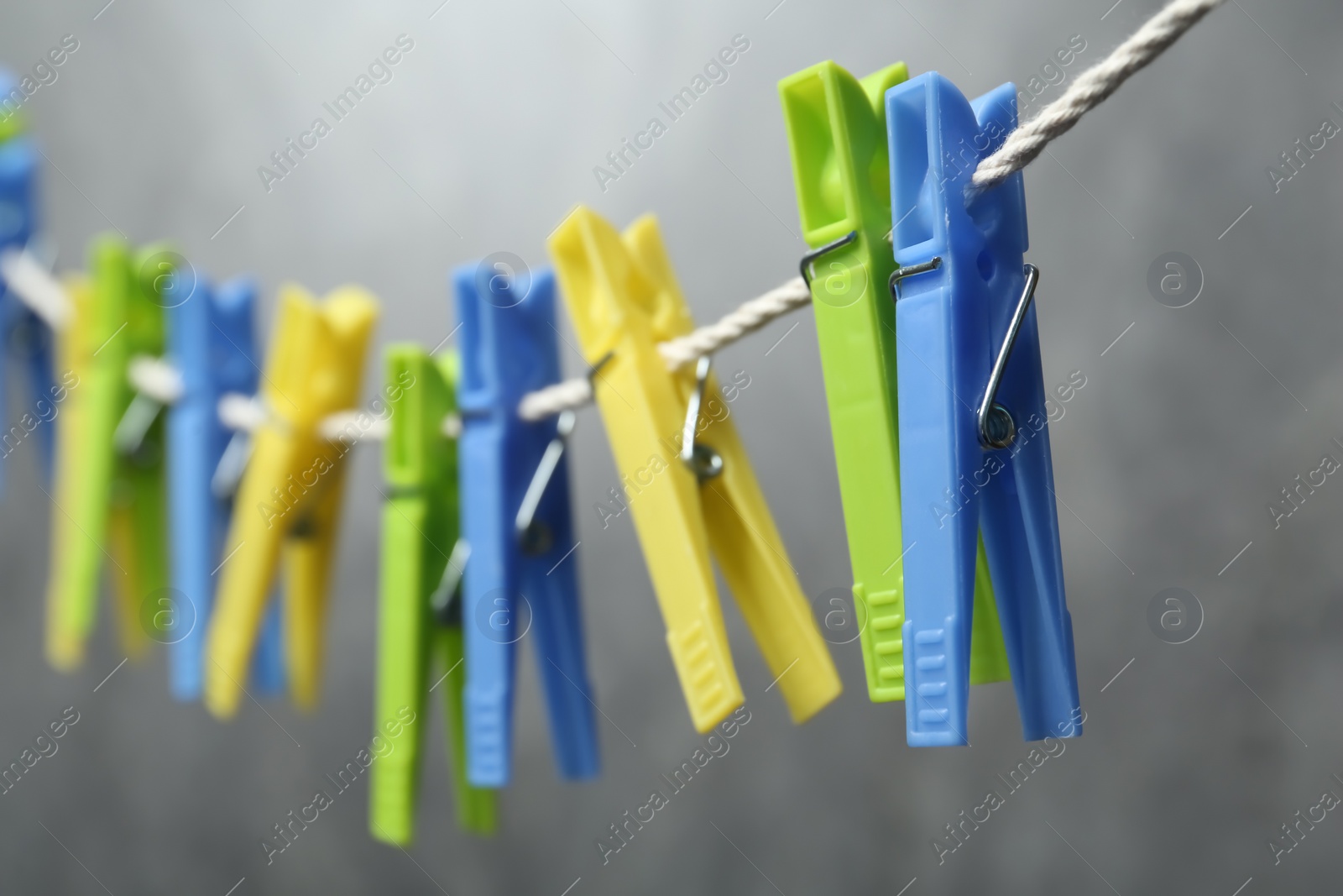 Photo of Green plastic clothespins on rope against grey background, closeup