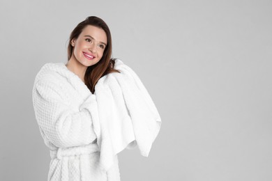 Photo of Young woman in bathrobe drying hair with towel on light grey background. Space for text
