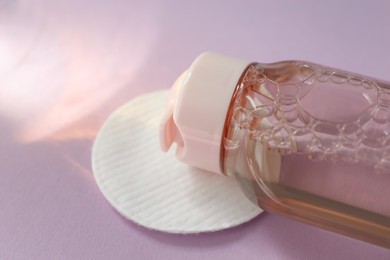 Photo of Bottle of micellar water and cotton pad on pink background, closeup