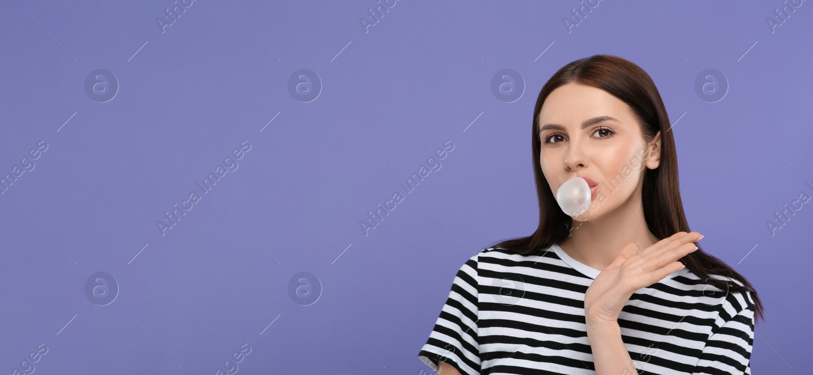 Photo of Beautiful woman blowing bubble gum on light purple background, space for text